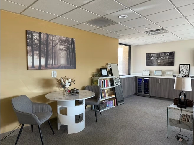 Progressive Movement Inc. waiting room with yellow accent wall, round table with chair, forest artwork, and reception desk